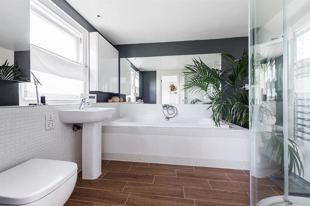 Inspiration for a large modern kids bathroom in London with flat-panel cabinets, white cabinets, a drop-in tub, an open shower, a wall-mount toilet, white tile, ceramic tile, grey walls, bamboo floors, a pedestal sink, tile benchtops, brown floor, a sliding shower screen and white benchtops.
