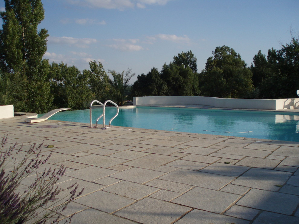 Photo of a mid-sized mediterranean rooftop rectangular infinity pool in Bordeaux with a water feature and natural stone pavers.