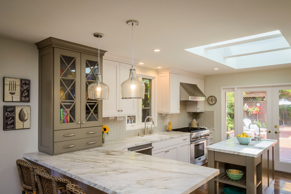 Inspiration for a mid-sized transitional galley open plan kitchen in San Francisco with an undermount sink, recessed-panel cabinets, white cabinets, marble benchtops, green splashback, stone slab splashback, stainless steel appliances, medium hardwood floors and with island.