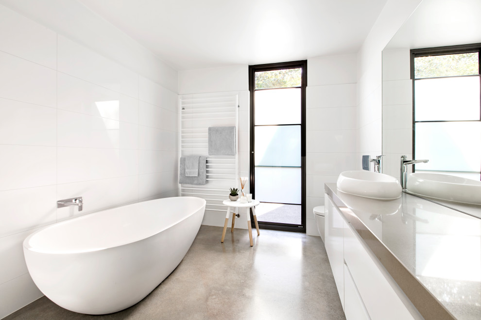 Photo of a large contemporary master bathroom in Melbourne with grey cabinets, a freestanding tub, a corner shower, a one-piece toilet, white tile, ceramic tile, yellow walls, concrete floors, a vessel sink, engineered quartz benchtops, a hinged shower door, grey benchtops, a single vanity and a floating vanity.