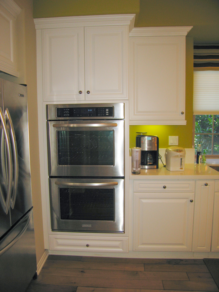Example of a mid-sized trendy galley light wood floor open concept kitchen design in Orange County with an undermount sink, raised-panel cabinets, white cabinets, quartzite countertops, green backsplash, stone slab backsplash, stainless steel appliances and an island