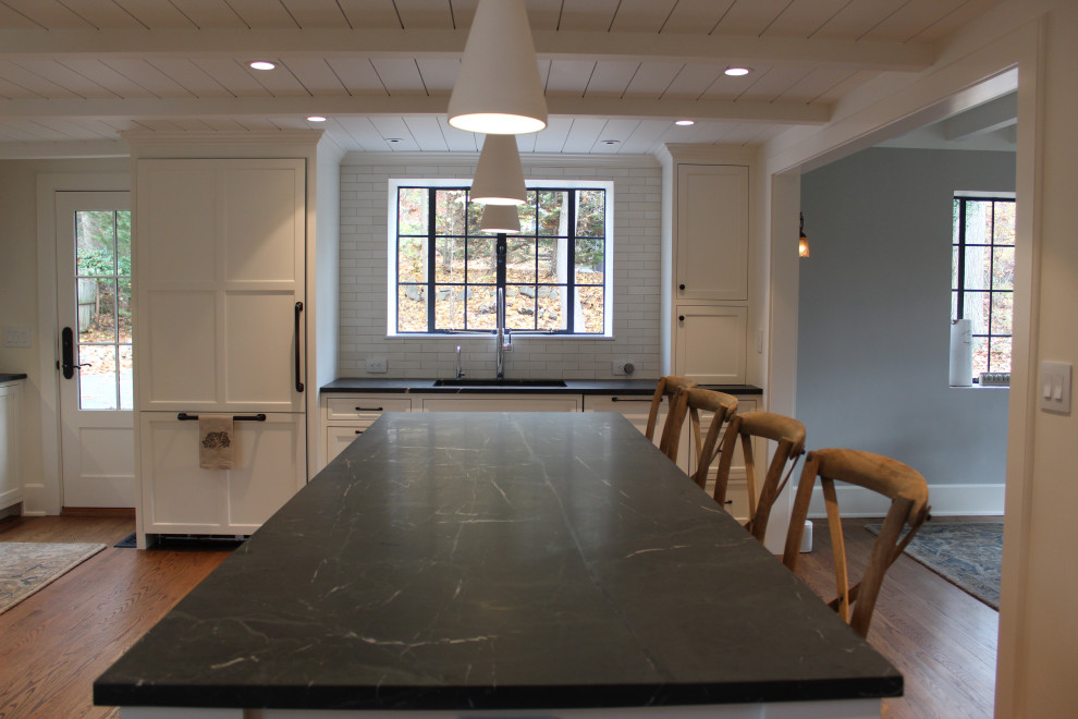 Klassisk inredning av ett stort grå grått kök, med en undermonterad diskho, luckor med infälld panel, vita skåp, bänkskiva i täljsten, vitt stänkskydd, stänkskydd i cementkakel, integrerade vitvaror, ljust trägolv, en köksö och brunt golv