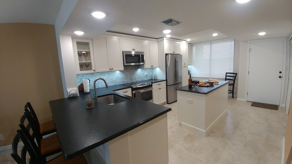 This is an example of a mid-sized tropical l-shaped open plan kitchen in Tampa with a single-bowl sink, shaker cabinets, white cabinets, granite benchtops, multi-coloured splashback, mosaic tile splashback, stainless steel appliances, porcelain floors, with island and beige floor.