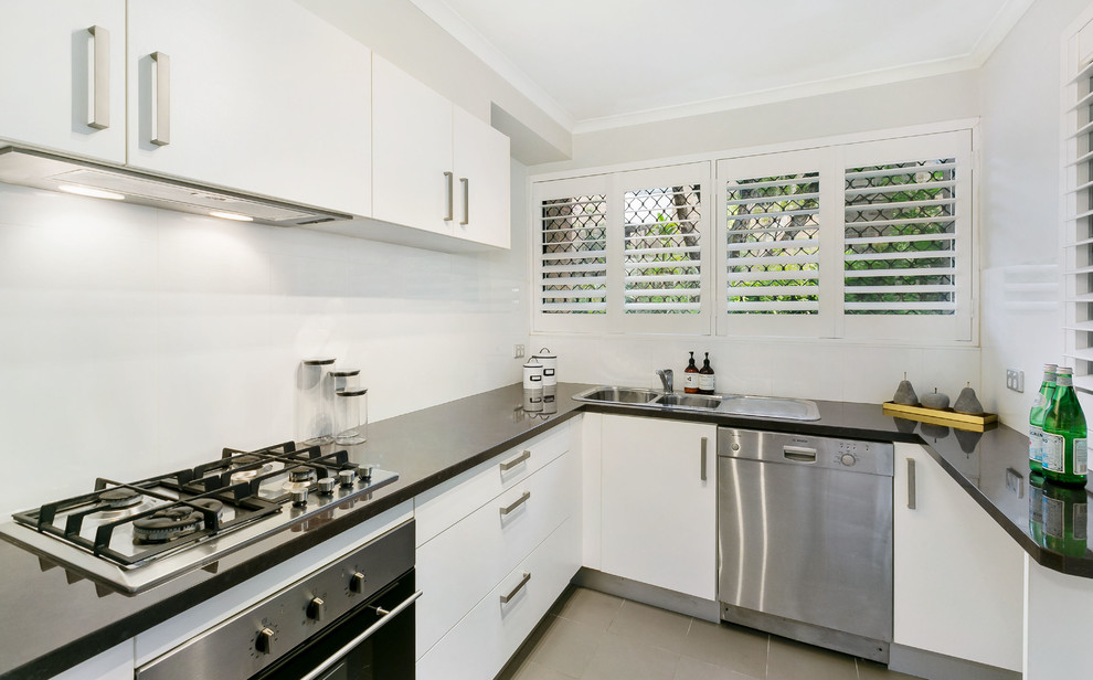 Inspiration for a small transitional l-shaped separate kitchen in Sydney with a double-bowl sink, white cabinets, quartz benchtops, white splashback, glass sheet splashback, stainless steel appliances and grey floor.
