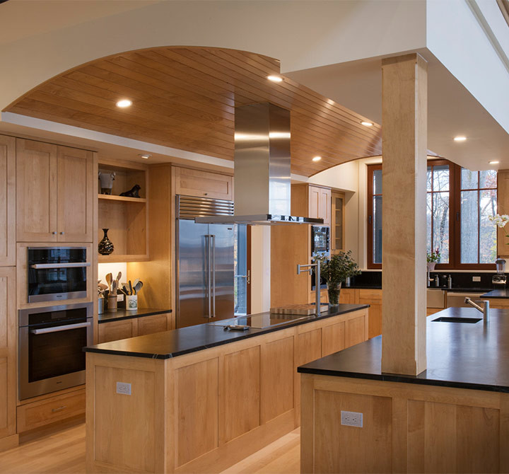 Example of a large transitional u-shaped light wood floor and beige floor enclosed kitchen design with shaker cabinets, light wood cabinets, two islands, an undermount sink, soapstone countertops, black backsplash, stone slab backsplash and stainless steel appliances