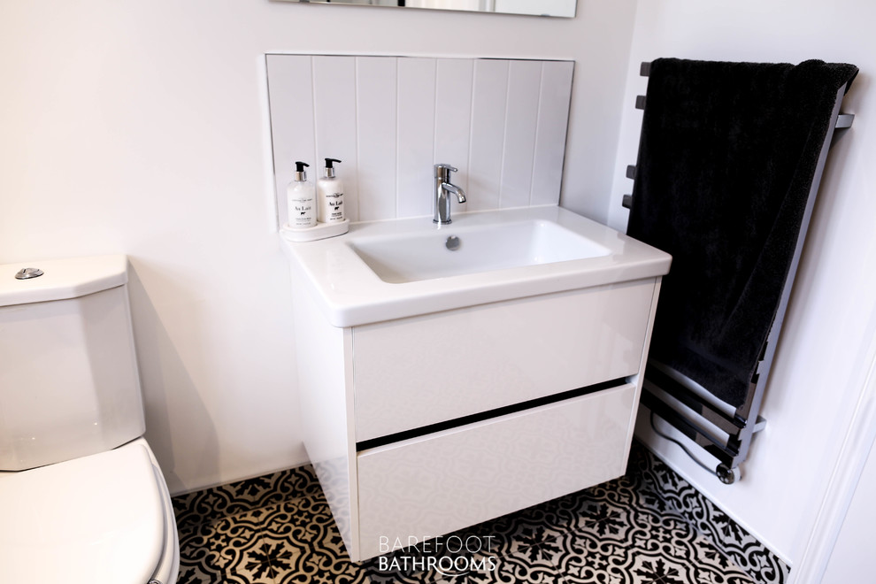Mid-sized traditional 3/4 wet room bathroom in Essex with furniture-like cabinets, white cabinets, a two-piece toilet, white tile, ceramic tile, white walls, ceramic floors, an integrated sink, solid surface benchtops, black floor, an open shower and white benchtops.