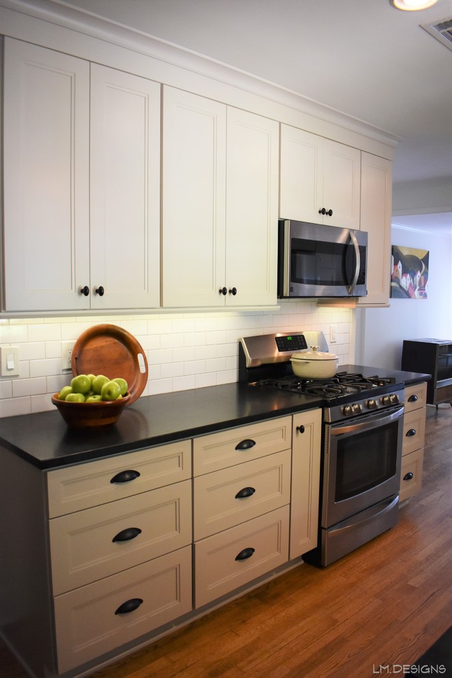 Transitional galley medium tone wood floor and brown floor kitchen photo with an undermount sink, recessed-panel cabinets, white cabinets, soapstone countertops, white backsplash, subway tile backsplash, stainless steel appliances and black countertops