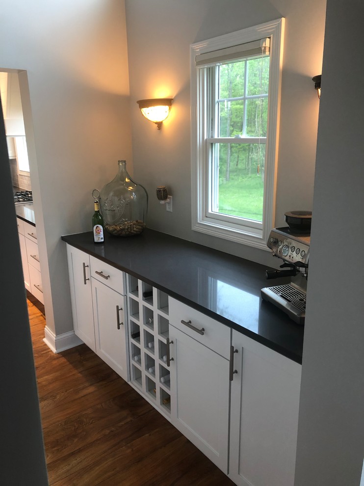 Kitchen - laminate floor and brown floor kitchen idea with a single-bowl sink, shaker cabinets, white cabinets, quartzite countertops, white backsplash, subway tile backsplash, stainless steel appliances, an island and gray countertops