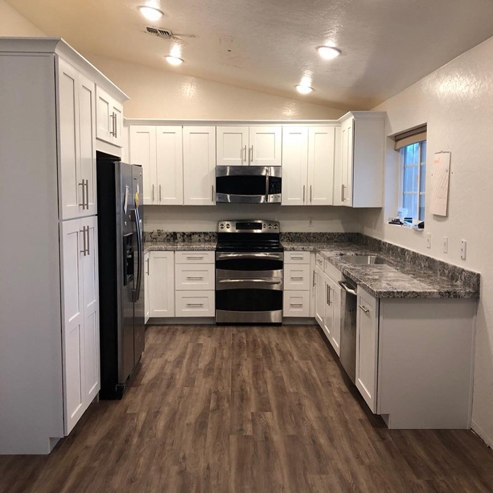 This is an example of a mid-sized transitional u-shaped eat-in kitchen in Phoenix with an undermount sink, shaker cabinets, white cabinets, granite benchtops, grey splashback, stone slab splashback, stainless steel appliances, vinyl floors, no island, brown floor and grey benchtop.