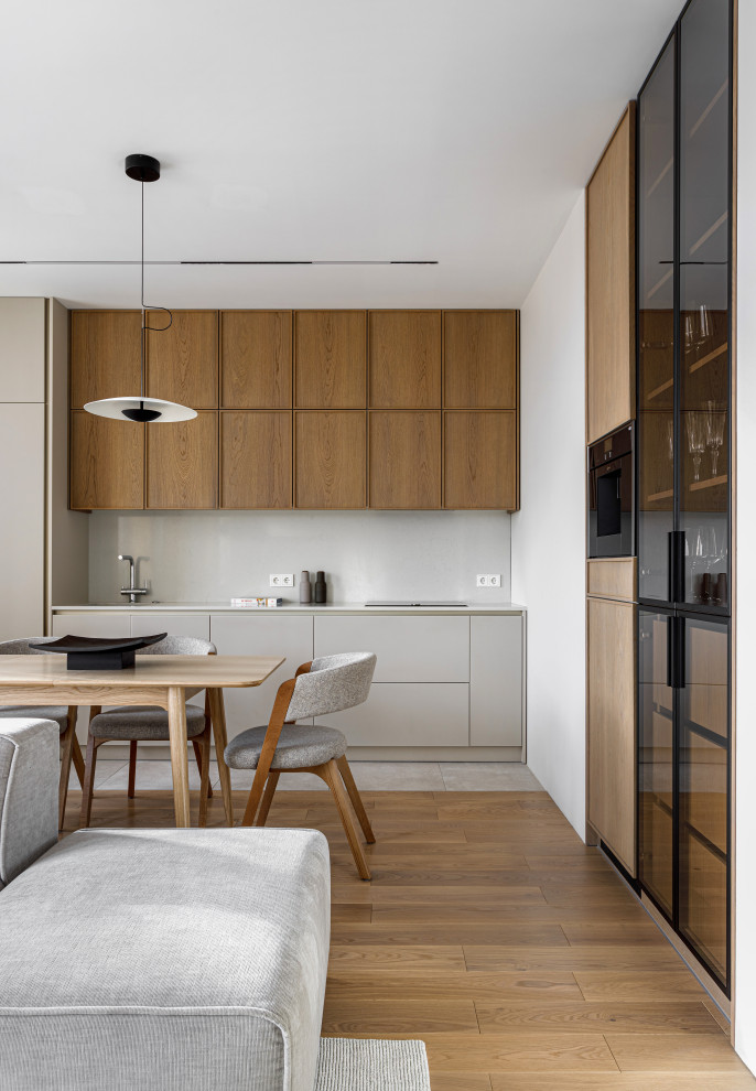 Design ideas for a mid-sized contemporary single-wall eat-in kitchen in Moscow with an undermount sink, raised-panel cabinets, medium wood cabinets, solid surface benchtops, beige splashback, black appliances, porcelain floors, beige floor and beige benchtop.