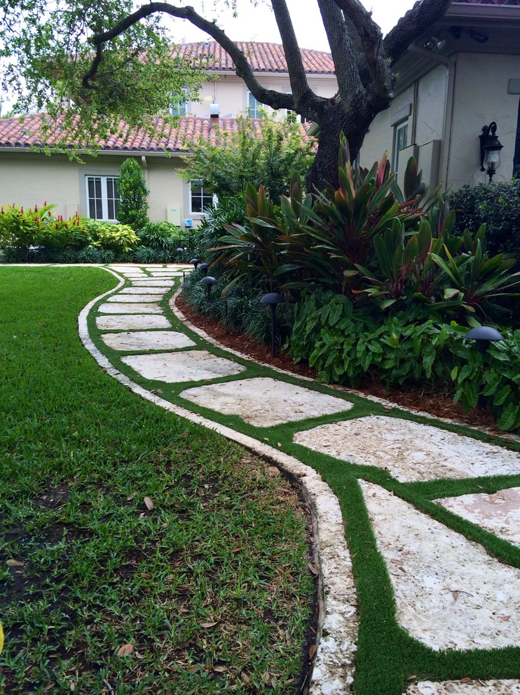 This is an example of a large contemporary side yard partial sun garden for summer in Miami with a garden path and natural stone pavers.