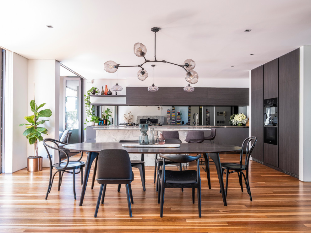 Contemporary kitchen in Sydney with open cabinets, stainless steel benchtops, mirror splashback, black appliances and brown floor.