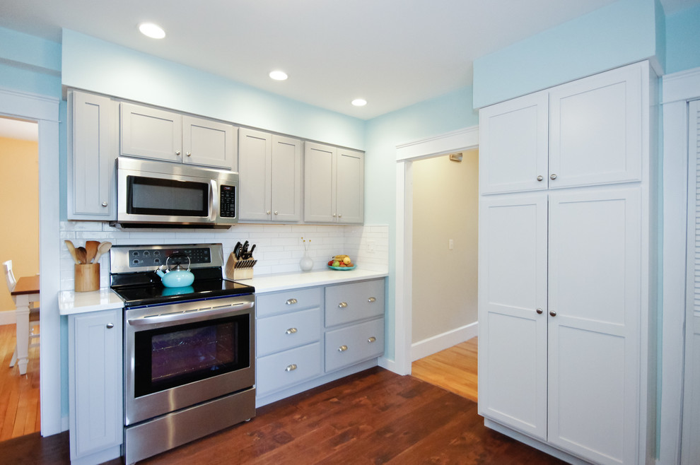 Inspiration for a mid-sized transitional galley medium tone wood floor and brown floor kitchen remodel in Boston with an undermount sink, shaker cabinets, gray cabinets, white backsplash, ceramic backsplash, stainless steel appliances and no island