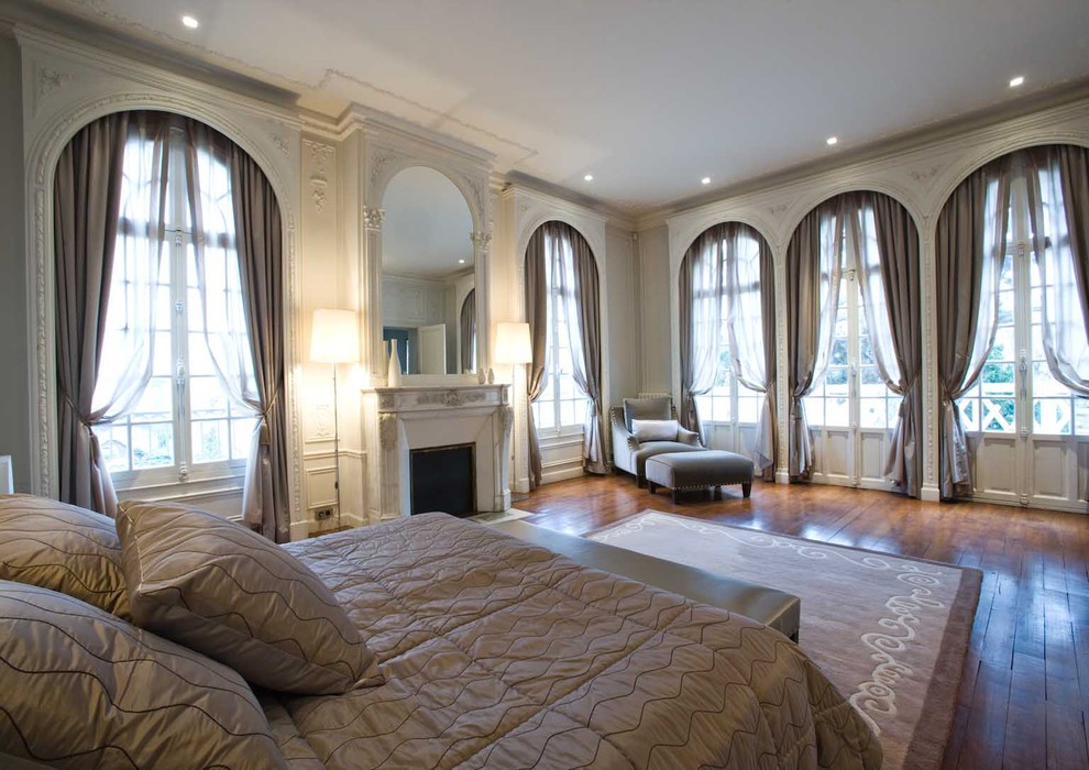 Photo of an expansive transitional master bedroom in Paris with beige walls, dark hardwood floors, a standard fireplace and a plaster fireplace surround.