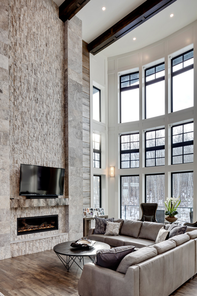 This is an example of an expansive transitional open concept living room in Calgary with grey walls, a stone fireplace surround, a wall-mounted tv, brown floor, medium hardwood floors and a ribbon fireplace.