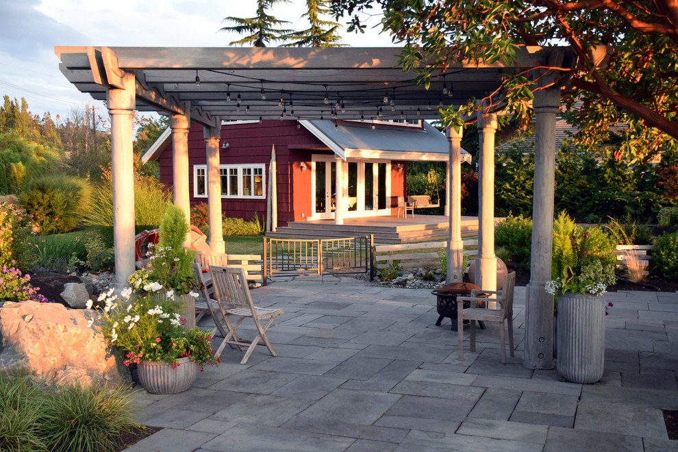 This is an example of a large country backyard patio in Seattle with natural stone pavers and a pergola.