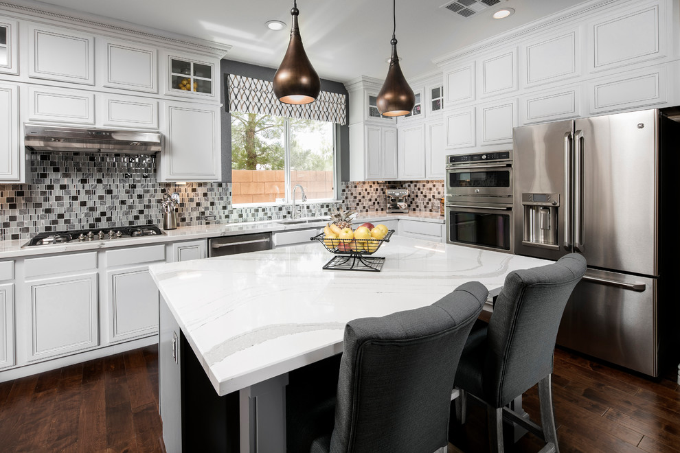 This is an example of a mid-sized transitional l-shaped eat-in kitchen in Las Vegas with an undermount sink, recessed-panel cabinets, white cabinets, quartz benchtops, stainless steel appliances, with island, mosaic tile splashback, dark hardwood floors, grey splashback and brown floor.