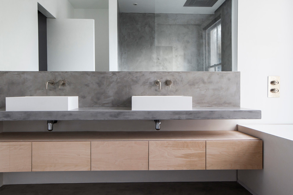 Photo of a mid-sized modern master bathroom in London with flat-panel cabinets, light wood cabinets, a freestanding tub, an open shower, a one-piece toilet, white walls, concrete floors, a console sink, concrete benchtops, grey floor and an open shower.