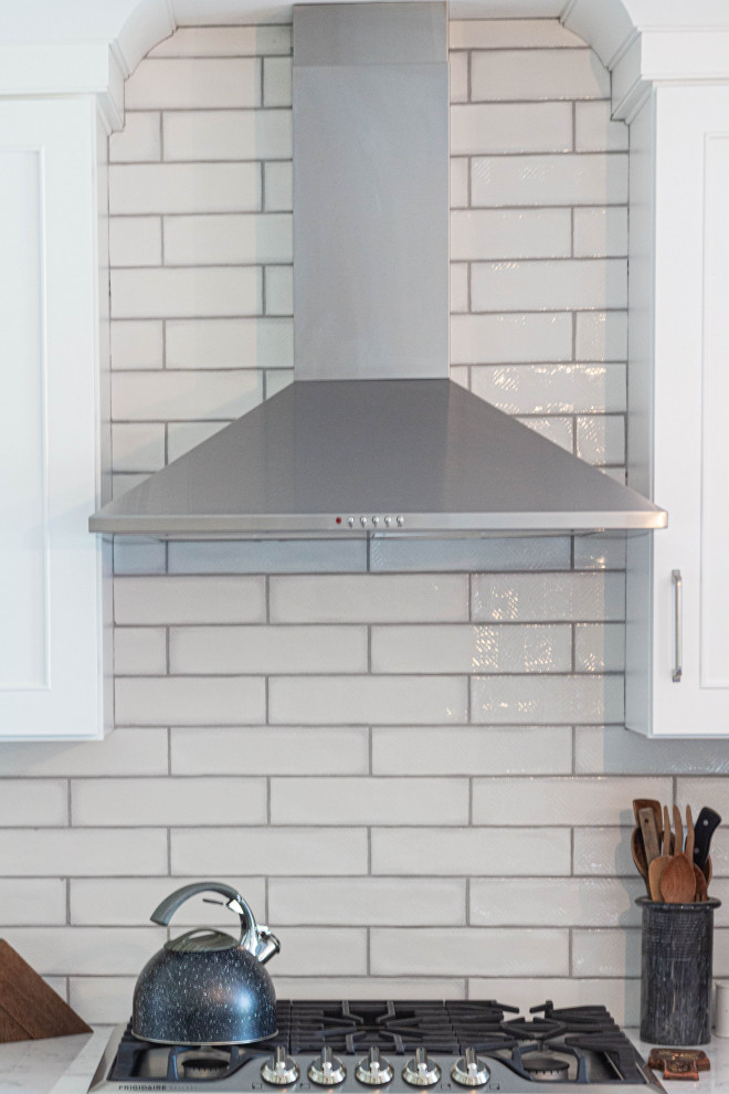 Example of a mid-sized transitional l-shaped porcelain tile and gray floor eat-in kitchen design with an undermount sink, flat-panel cabinets, white cabinets, quartz countertops, white backsplash, subway tile backsplash, stainless steel appliances, an island and white countertops