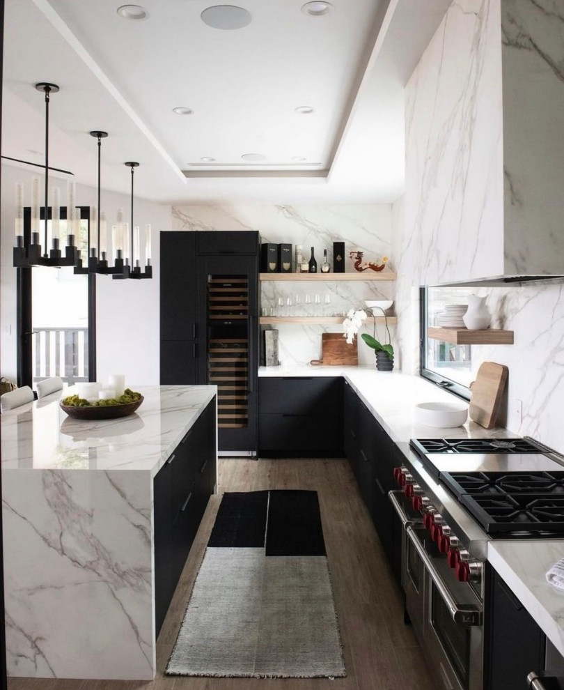 Photo of a large l-shaped open plan kitchen in Dallas with flat-panel cabinets, black cabinets, marble benchtops, white splashback, stone slab splashback, coloured appliances, light hardwood floors, with island, brown floor and white benchtop.