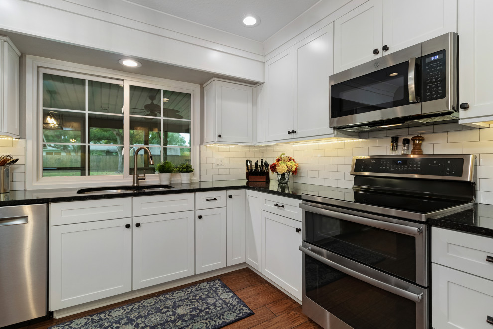 Large traditional u-shaped eat-in kitchen in Tampa with a double-bowl sink, shaker cabinets, white cabinets, quartz benchtops, white splashback, ceramic splashback, stainless steel appliances, medium hardwood floors, no island, brown floor and black benchtop.