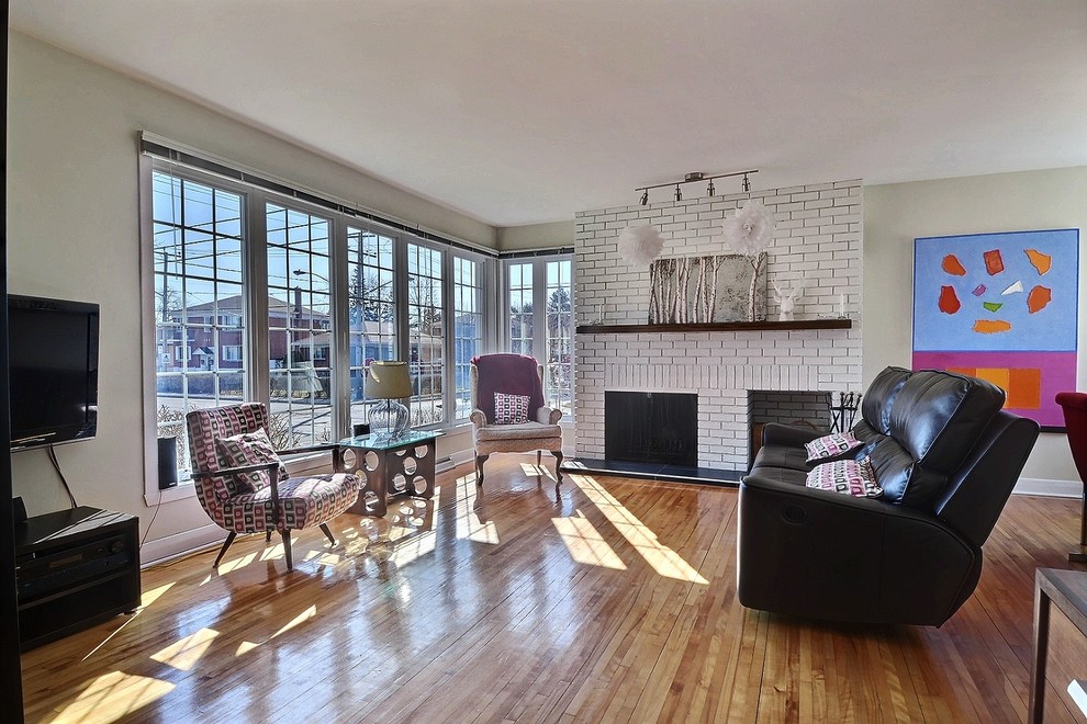 This is an example of a mid-sized contemporary formal open concept living room in Montreal with beige walls, light hardwood floors, a hanging fireplace, a brick fireplace surround and beige floor.