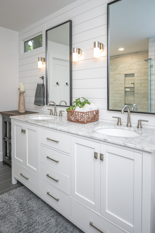Photo of a mid-sized country master bathroom in Raleigh with shaker cabinets, white cabinets, a double shower, a two-piece toilet, white tile, porcelain tile, white walls, porcelain floors, an undermount sink, marble benchtops, grey floor, a hinged shower door, grey benchtops, an enclosed toilet, a double vanity, a freestanding vanity and planked wall panelling.