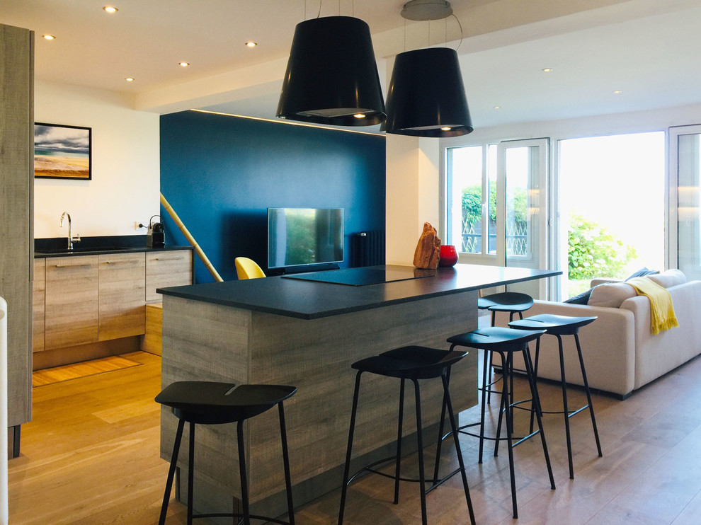 Large contemporary l-shaped eat-in kitchen in Rennes with an integrated sink, beaded inset cabinets, light wood cabinets, granite benchtops, black splashback, limestone splashback, black appliances, light hardwood floors, with island, brown floor and black benchtop.