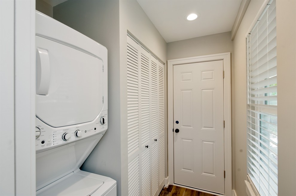 Design ideas for a small contemporary galley utility room in Tampa with louvered cabinets, white cabinets, beige walls, medium hardwood floors, a stacked washer and dryer and grey floor.