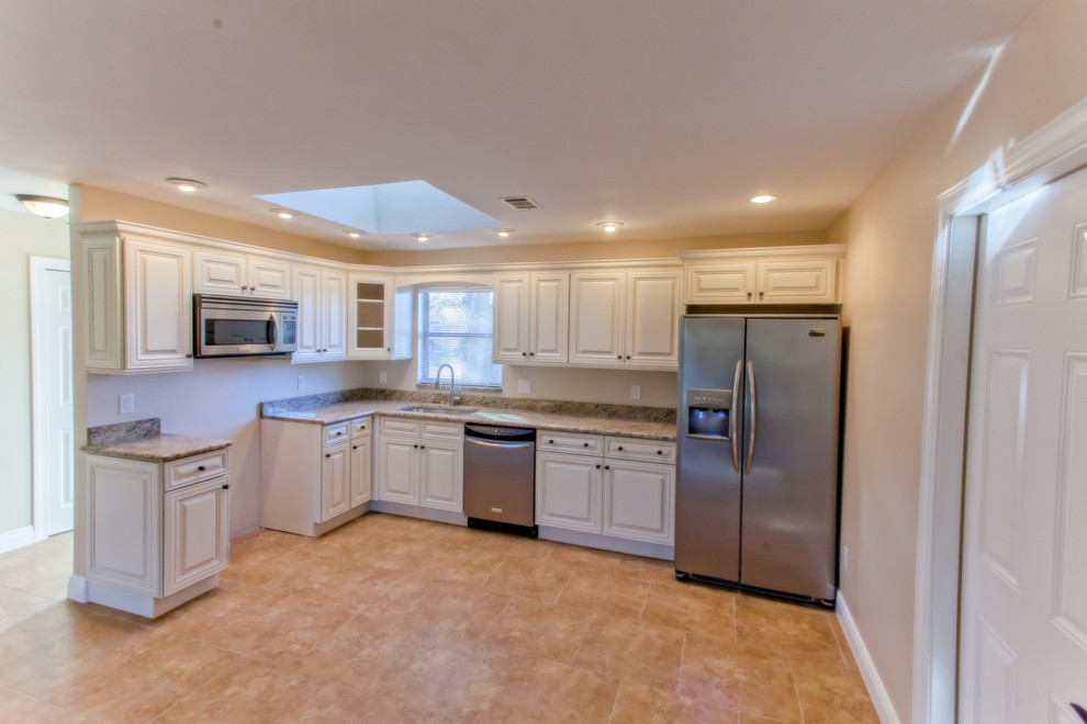 This is an example of a mid-sized transitional l-shaped open plan kitchen in Miami with an undermount sink, raised-panel cabinets, white cabinets, granite benchtops, stainless steel appliances, laminate floors, no island, brown floor and multi-coloured benchtop.