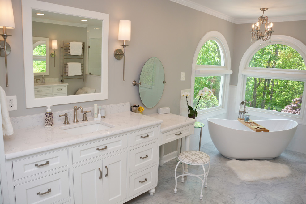 This is an example of a large traditional master bathroom in Baltimore with recessed-panel cabinets, white cabinets, a freestanding tub, an alcove shower, a two-piece toilet, white tile, grey walls, an undermount sink, engineered quartz benchtops, grey floor, a hinged shower door, white benchtops, a shower seat, a double vanity and a freestanding vanity.