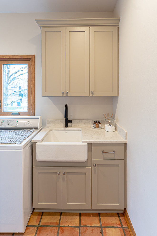 Photo of a large traditional single-wall utility room in Milwaukee with an undermount sink, shaker cabinets, beige cabinets, quartz benchtops, beige splashback, engineered quartz splashback, white walls, terra-cotta floors, a side-by-side washer and dryer, multi-coloured floor and beige benchtop.