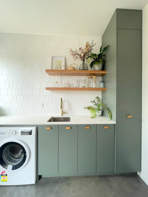 Photo of a mid-sized contemporary galley dedicated laundry room in Dunedin with a single-bowl sink, flat-panel cabinets, green cabinets, quartz benchtops, white splashback, porcelain splashback, white walls, concrete floors, a side-by-side washer and dryer, grey floor and white benchtop.