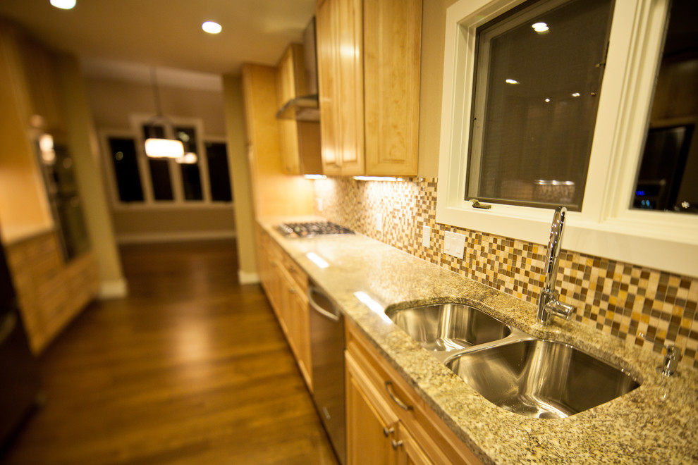 Inspiration for a mid-sized transitional galley medium tone wood floor and brown floor enclosed kitchen remodel in Denver with a double-bowl sink, raised-panel cabinets, medium tone wood cabinets, granite countertops, multicolored backsplash, mosaic tile backsplash, stainless steel appliances and no island
