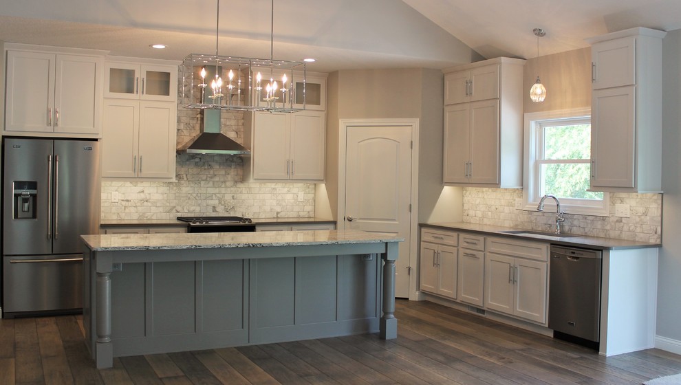 This is an example of a large traditional l-shaped open plan kitchen in Other with a submerged sink, flat-panel cabinets, grey cabinets, engineered stone countertops, white splashback, marble splashback, stainless steel appliances, medium hardwood flooring, an island and grey floors.