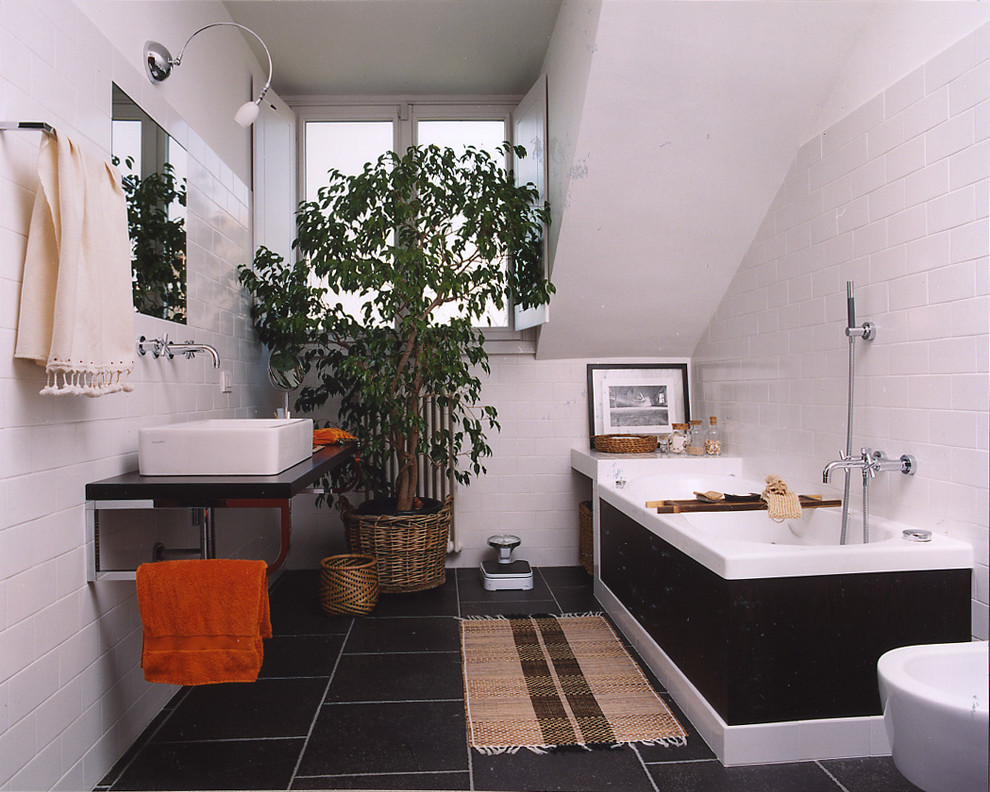 This is an example of a mid-sized country master bathroom in Milan with an alcove tub, a shower/bathtub combo, a bidet, white walls, ceramic floors, a wall-mount sink, black floor and an open shower.