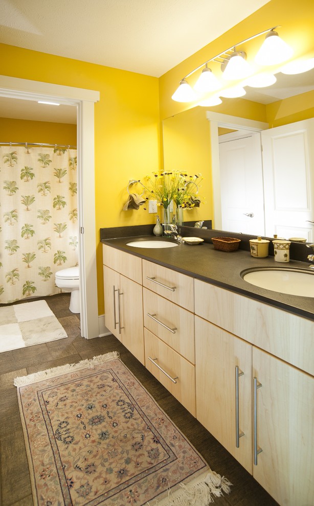 This is an example of a contemporary kids bathroom with flat-panel cabinets, light wood cabinets, an alcove tub, a shower/bathtub combo, a two-piece toilet, yellow walls, an undermount sink, a shower curtain, black benchtops, a double vanity and a built-in vanity.