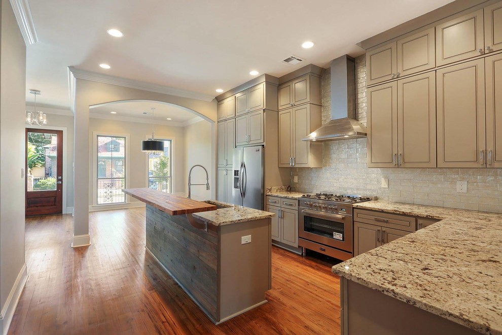 Photo of a large transitional single-wall separate kitchen in New Orleans with an undermount sink, louvered cabinets, beige cabinets, granite benchtops, beige splashback, brick splashback, stainless steel appliances, medium hardwood floors, with island and brown floor.