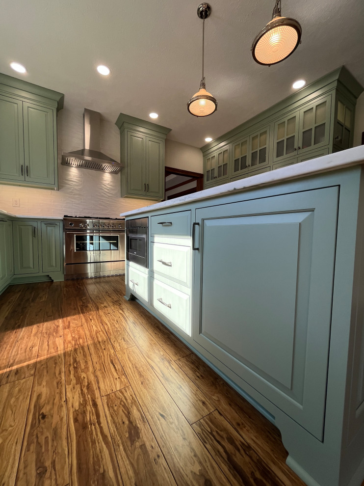This is an example of a large u-shaped kitchen pantry in Indianapolis with a submerged sink, beaded cabinets, quartz worktops, white splashback, ceramic splashback, stainless steel appliances, medium hardwood flooring, an island, brown floors and white worktops.