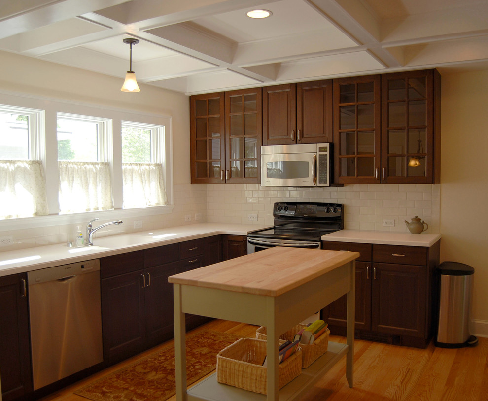 Mid-sized transitional medium tone wood floor eat-in kitchen photo in Chicago with an integrated sink, raised-panel cabinets, dark wood cabinets, solid surface countertops, white backsplash, subway tile backsplash, stainless steel appliances and an island