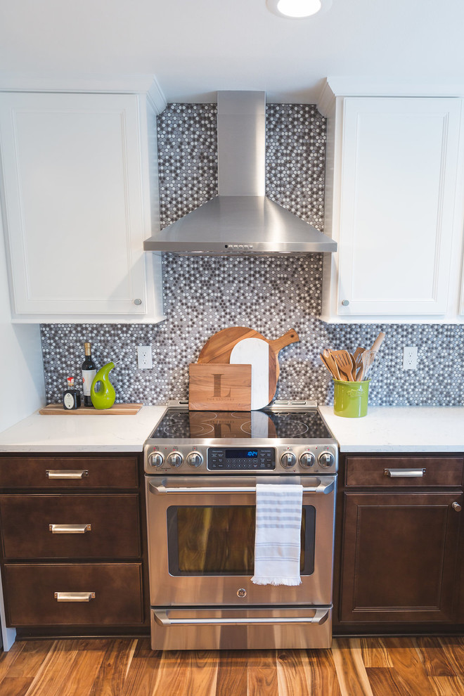 This is an example of a mid-sized transitional u-shaped eat-in kitchen in Seattle with a farmhouse sink, recessed-panel cabinets, white cabinets, quartzite benchtops, grey splashback, mosaic tile splashback, stainless steel appliances, medium hardwood floors, a peninsula and brown floor.
