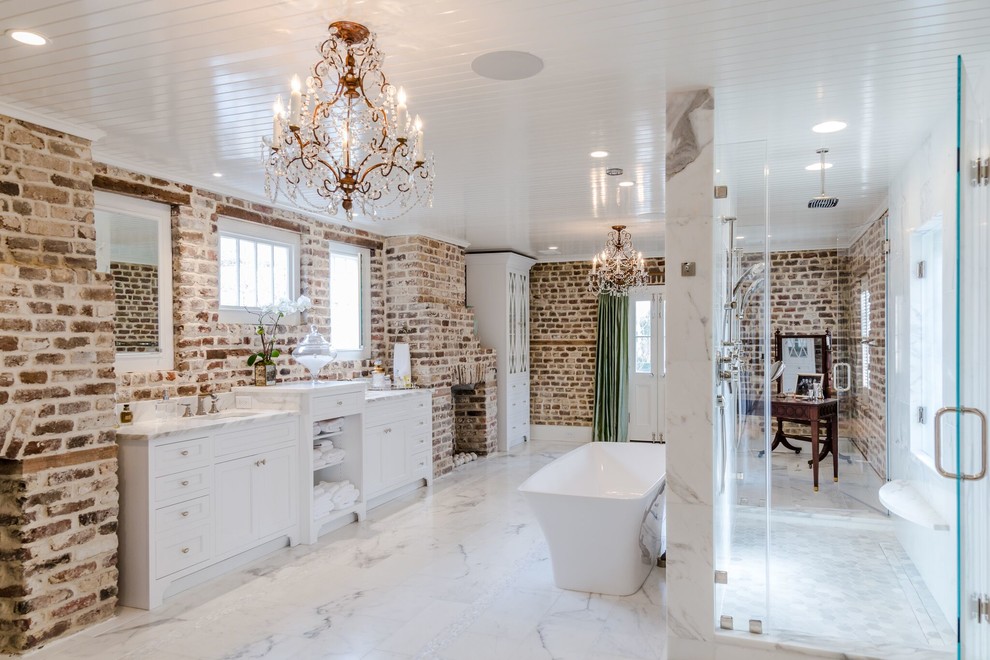 This is an example of a large transitional master bathroom in Charleston with white cabinets, a freestanding tub, a double shower, a one-piece toilet, multi-coloured walls, marble floors, an undermount sink, marble benchtops, white floor, a hinged shower door, white tile and recessed-panel cabinets.