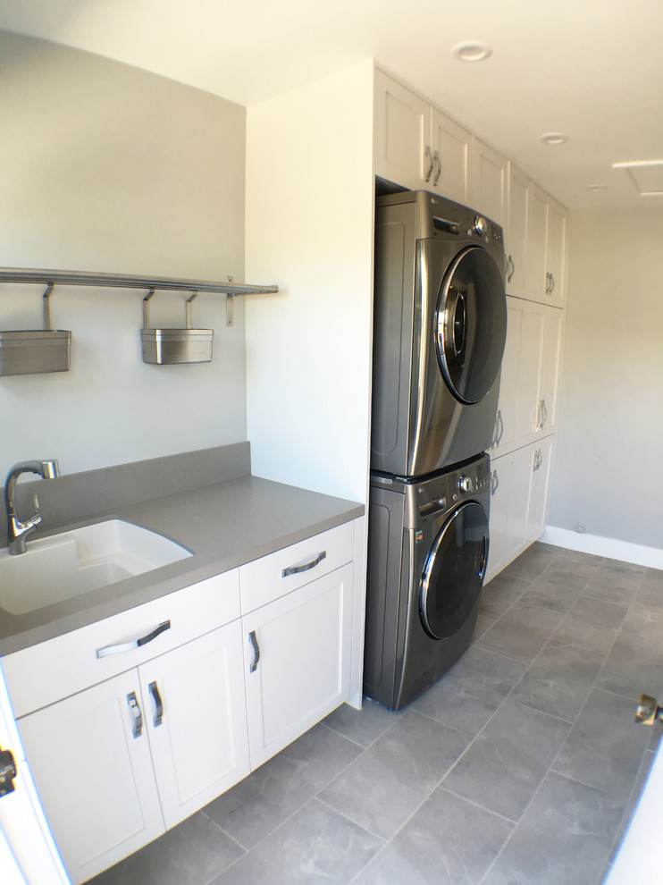Mid-sized transitional single-wall utility room in Los Angeles with an utility sink, shaker cabinets, white cabinets, quartz benchtops, grey walls, porcelain floors and a stacked washer and dryer.