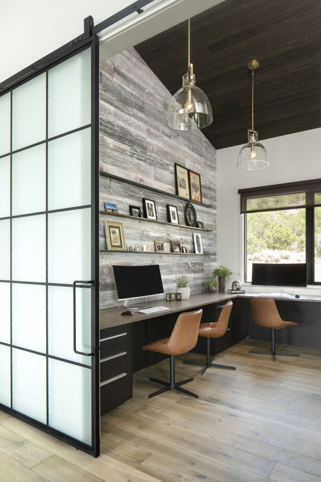 Inspiration for a large industrial home studio in Denver with white walls, light hardwood floors, a built-in desk, brown floor, vaulted and wood walls.