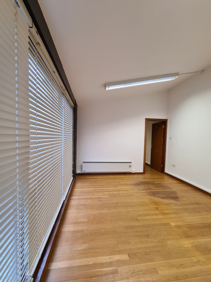Aménagement d'un grand bureau atelier moderne avec un mur blanc, parquet foncé, un sol marron et un plafond décaissé.