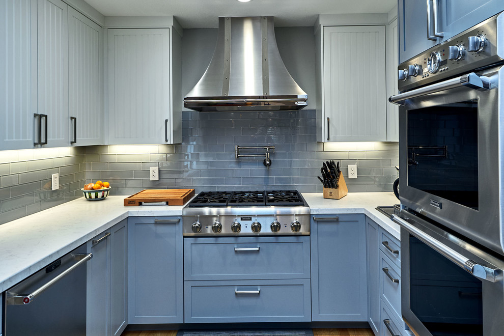 Photo of a mid-sized transitional u-shaped open plan kitchen in San Francisco with an undermount sink, louvered cabinets, blue cabinets, marble benchtops, grey splashback, glass tile splashback, stainless steel appliances, medium hardwood floors, no island, brown floor and white benchtop.