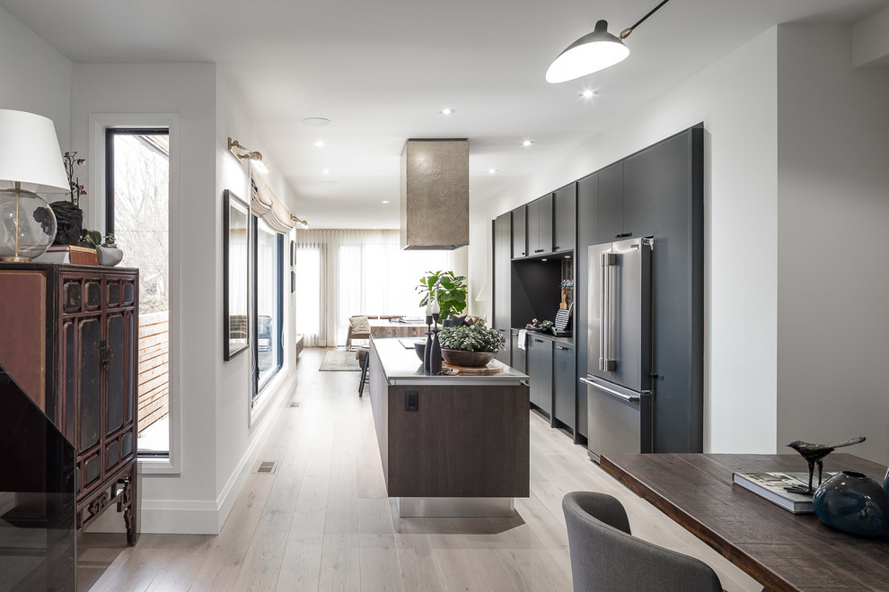 This is an example of a mid-sized modern galley eat-in kitchen in Ottawa with an undermount sink, flat-panel cabinets, grey cabinets, stainless steel benchtops, grey splashback, stainless steel appliances, light hardwood floors and with island.