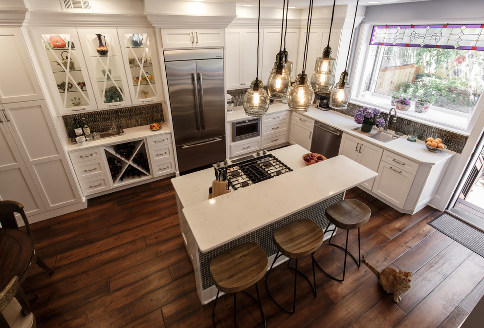 Mid-sized eclectic l-shaped eat-in kitchen in Philadelphia with an undermount sink, shaker cabinets, quartz benchtops, grey splashback, glass tile splashback, stainless steel appliances, dark hardwood floors, with island, brown floor and white cabinets.