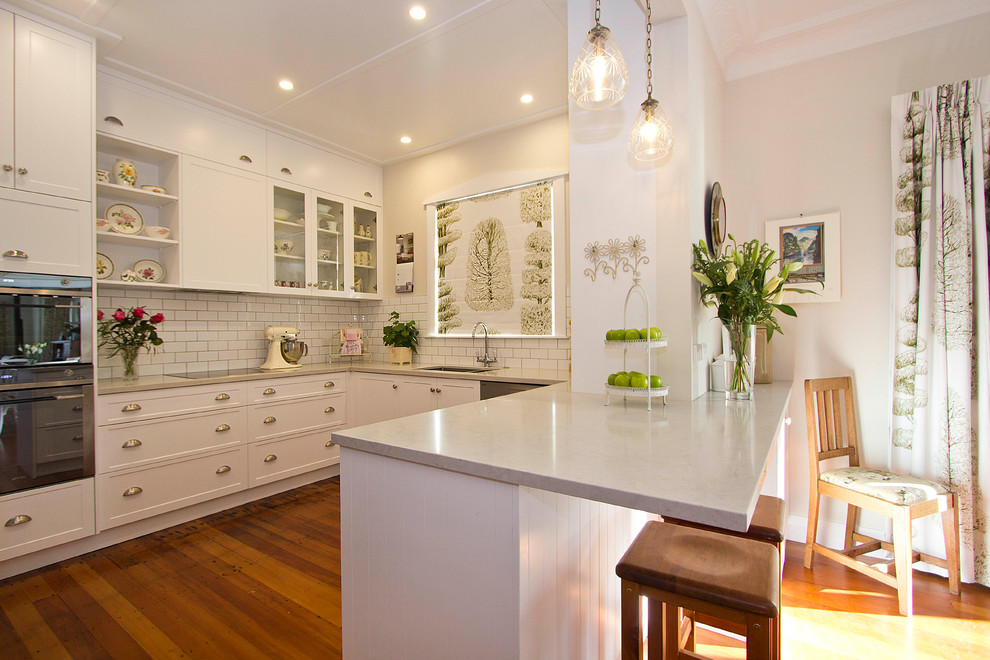 Design ideas for a small traditional u-shaped eat-in kitchen in Wellington with an undermount sink, shaker cabinets, white cabinets, granite benchtops, white splashback, subway tile splashback, stainless steel appliances, medium hardwood floors and a peninsula.