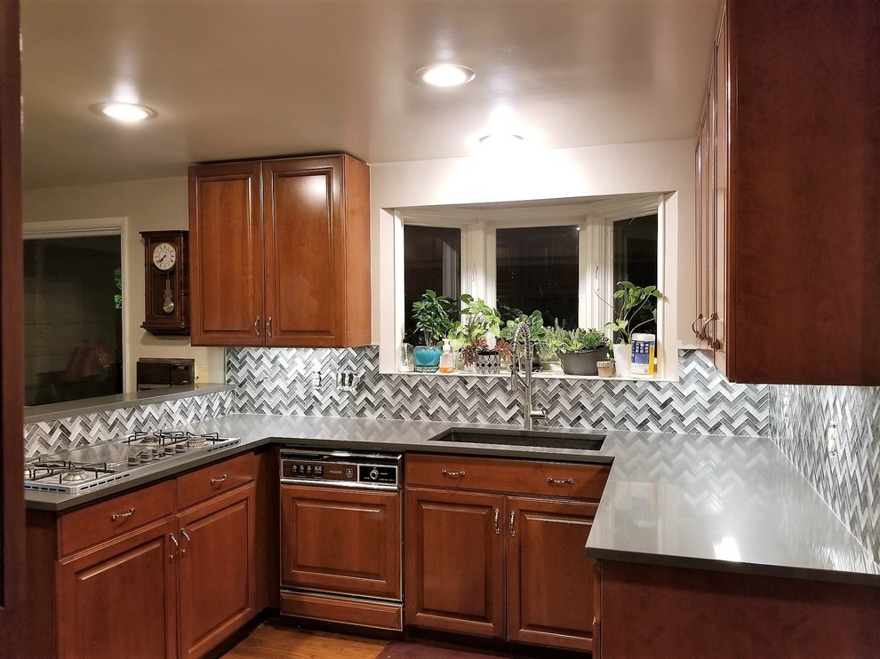Inspiration for a small traditional u-shaped open plan kitchen in Seattle with an undermount sink, raised-panel cabinets, medium wood cabinets, solid surface benchtops, grey splashback, glass tile splashback, stainless steel appliances, medium hardwood floors, a peninsula, brown floor and grey benchtop.